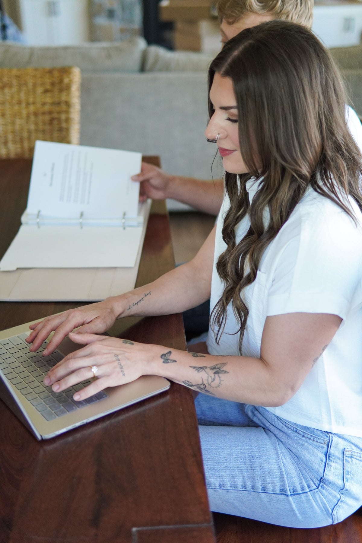 Newlywed couple sitting together at their kitchen table surrounded by post-wedding paperwork and planning documents, organizing their first year of marriage