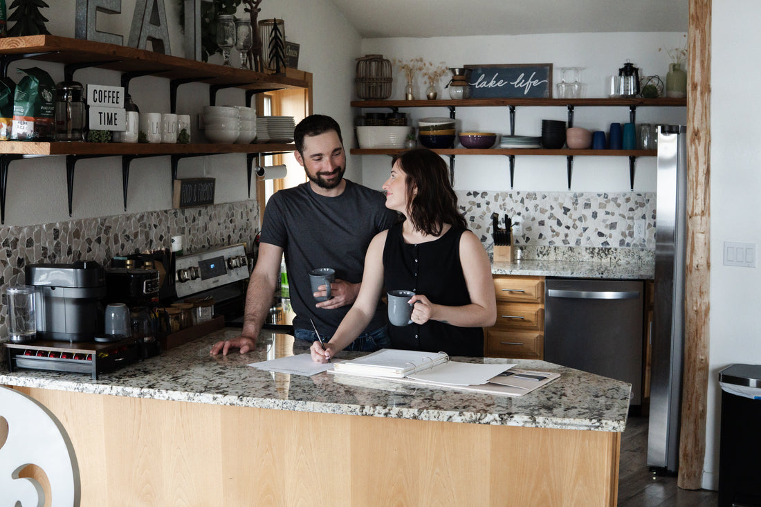 Newlywed couple creating their first monthly budget together at a kitchen table with bills, a laptop, and a notebook.